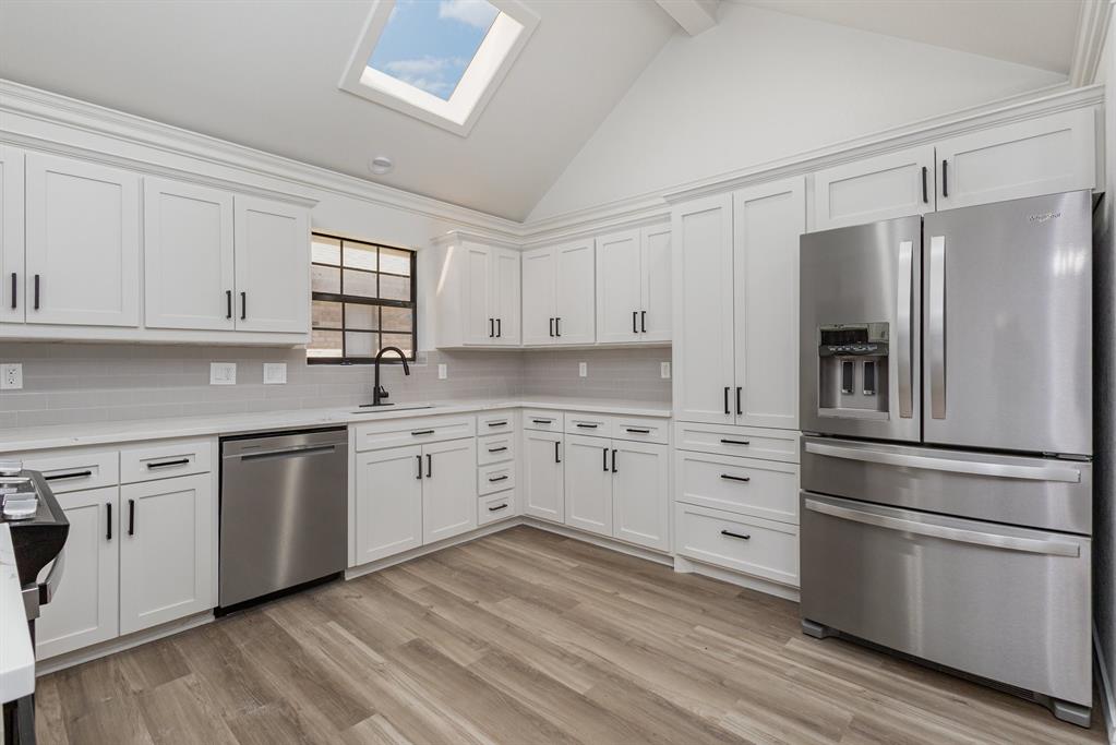 922 Sycamore Creek Road Allen, TX 75002 - Photo 15 of 38 Kitchen featuring stainless steel appliances, white cabinetry, light wood-type flooring, a skylight, and high vaulted ceiling