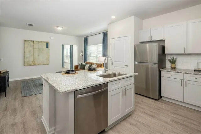 a kitchen with a sink dishwasher a refrigerator and white cabinets with wooden floor