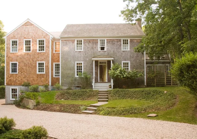 a view of a brick house with a yard plants and large tree
