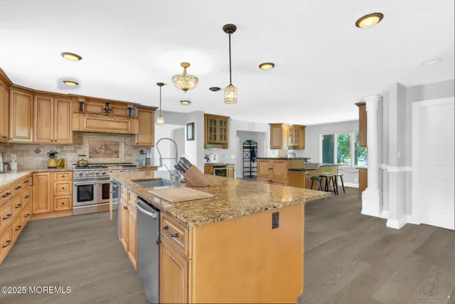 a kitchen with kitchen island granite countertop a stove a sink a refrigerator and white cabinets with wooden floor