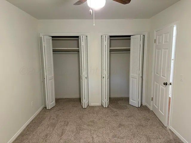 an empty room with chandelier fan and windows