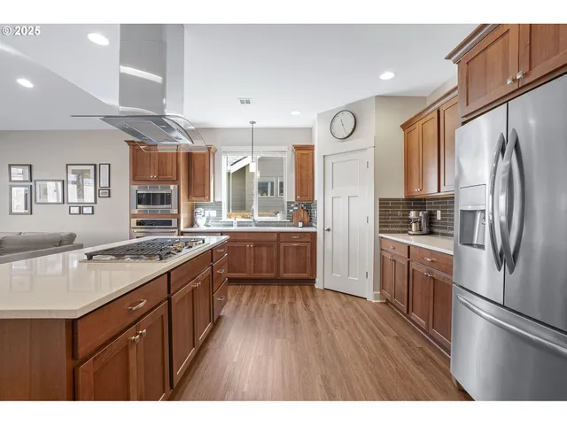 a kitchen with stainless steel appliances granite countertop a refrigerator a sink dishwasher a stove and white countertops with wooden floor