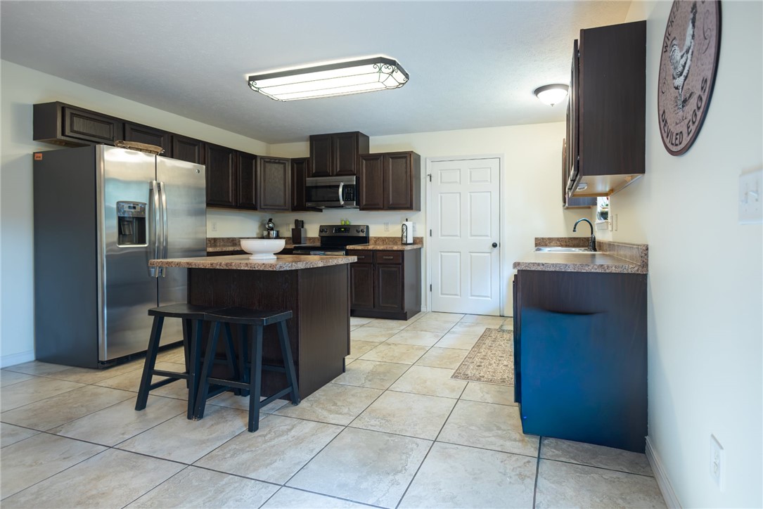 437 Gip Annie Road West Harrison, AR 72601 - Photo 8 of 21 Kitchen featuring dark wood-finish cabinetry, a central island with countertop seating, stainless steel appliances, and tile flooring