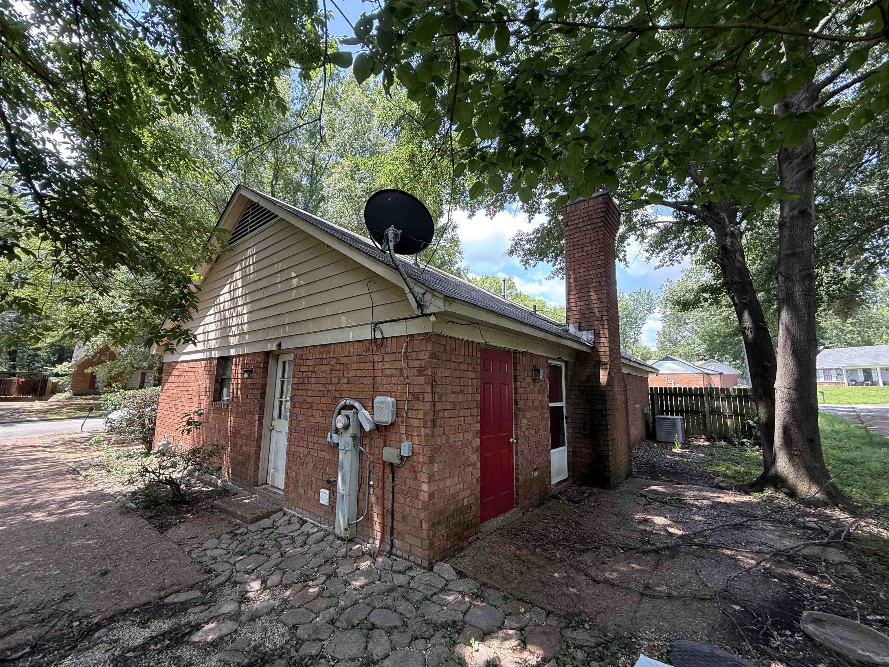 6420 Saginaw Road Memphis, TN 38134 - Photo 36 of 38 Brick exterior with a prominent brick chimney, accompanied by a red entry door, a white side door, and a partially fenced yard