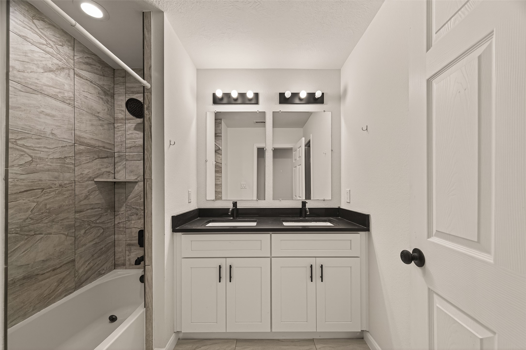 4302 Hirsch Road, Unit B Houston, TX 77026 - Photo 15 of 19 This modern family bathroom features a sleek design with a double vanity, black countertops, and ample storage. The shower-tub combo is lined with elegant, earthy tiles, and the space is well-lit with contemporary fixtures.