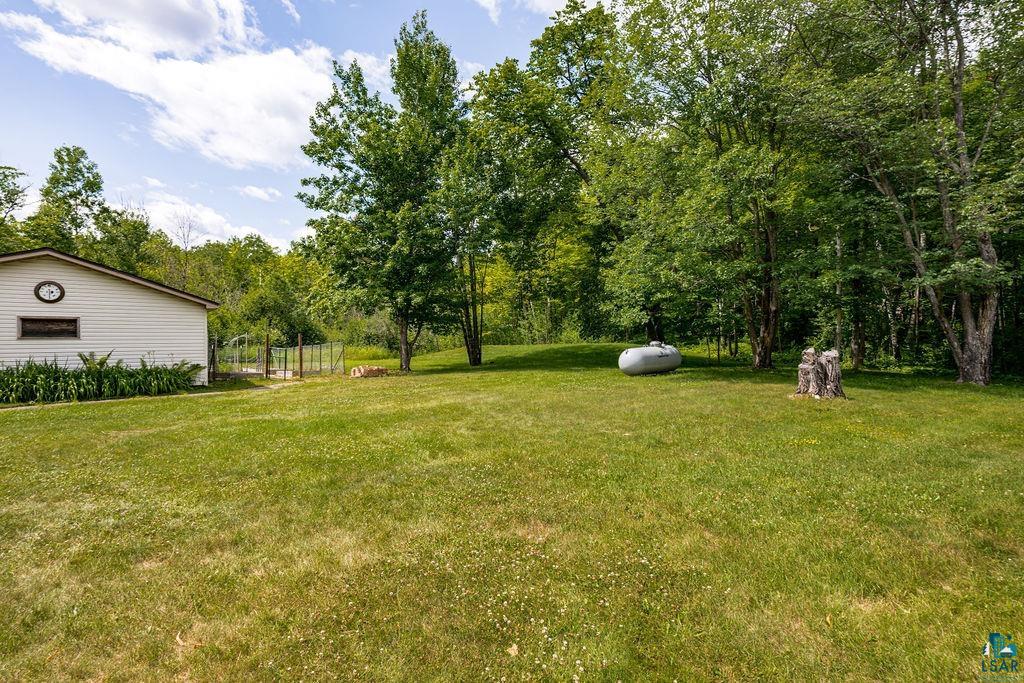 5025 Reid Road Duluth, MN 55803 - Photo 39 of 51 Expansive green lawn surrounded by mature trees, featuring a white siding structure with dark trim, a fenced area, and a large propane tank