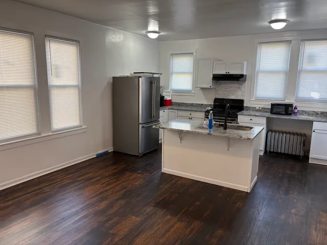 a kitchen with kitchen island wooden floors white cabinets and stainless steel appliances