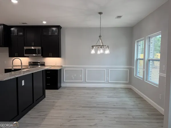 a large kitchen with stainless steel appliances granite countertop a stove a sink dishwasher a microwave oven and a dining table with wooden floor