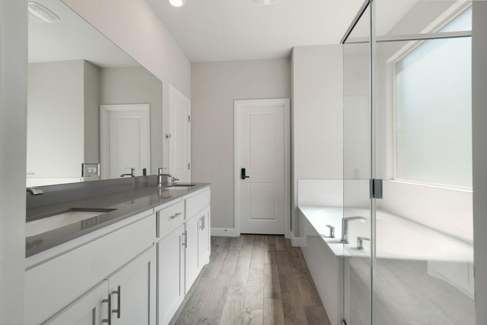 1112 Croxley Way Justin, TX 76247 - Photo 8 of 18 Bathroom featuring a dual vanity with a gray countertop, an integrated soaking tub, a frameless glass shower enclosure, wood-look flooring, and a frosted privacy window