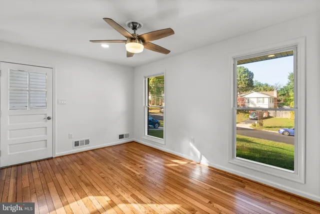 an empty room with wooden floor fan and windows