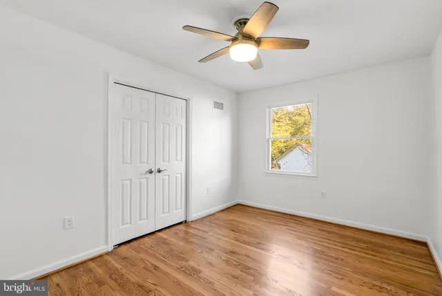 an empty room with wooden floor fan and windows