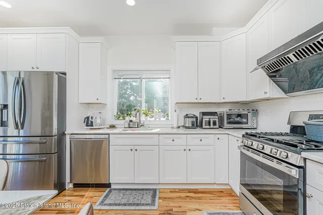 a kitchen with stainless steel appliances a stove top oven a sink dishwasher and white cabinets with wooden floor