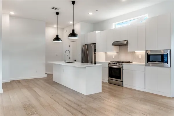 a large kitchen with stainless steel appliances a large counter top a stove a sink and a refrigerator