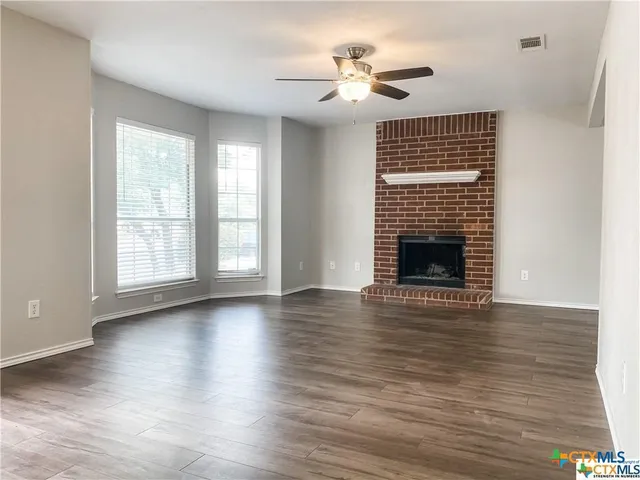a view of an empty room with wooden floor fireplace and a window