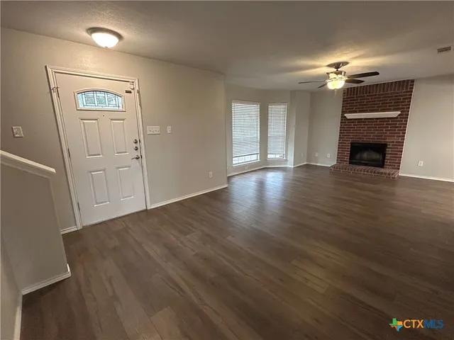 a view of a livingroom with a fireplace a ceiling fan and wooden floor