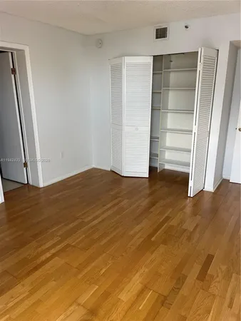 a view of an empty room with wooden floor and closet