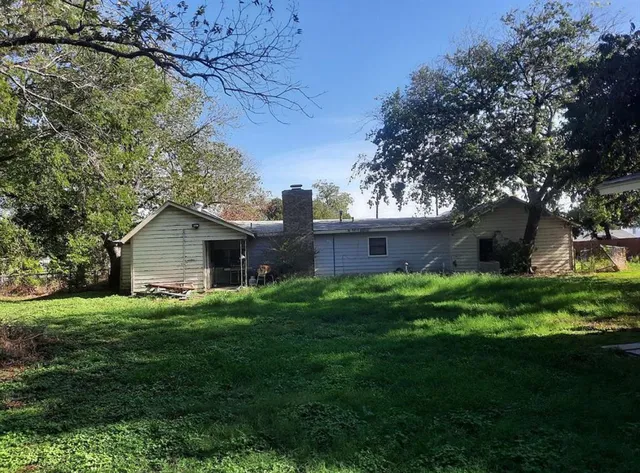 a backyard of a house with plants and large tree
