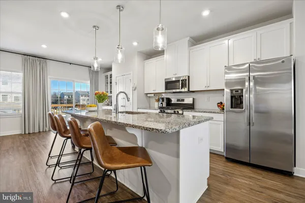 a kitchen with stainless steel appliances granite countertop a refrigerator a stove a sink a dining table and chairs with wooden floor