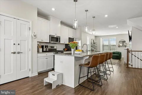 a kitchen with stainless steel appliances granite countertop a stove a sink a microwave a refrigerator and white cabinets with wooden floor