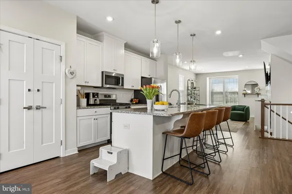 a kitchen with stainless steel appliances granite countertop a stove a sink a microwave a refrigerator and white cabinets with wooden floor