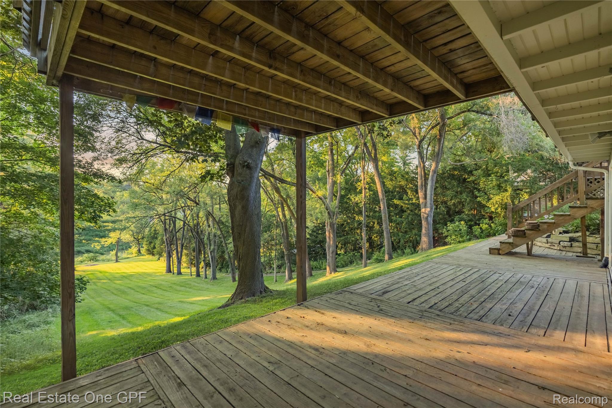5068 Atkins Road North Street, MI 48049 - Photo 56 of 78 Expansive wood deck with a built-in staircase and wooden railings, overlooking a large grassy area and mature trees