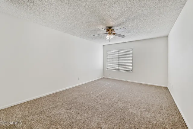 an empty room with chandelier fan and windows