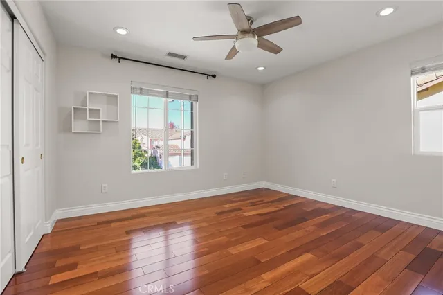 a view of an empty room with wooden floor and a ceiling fan