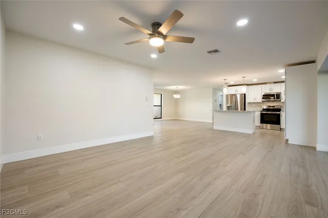 an empty room with wooden floor a ceiling fan and kitchen view
