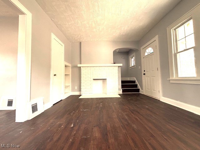Unfurnished living room featuring a brick fireplace, baseboards, visible vents, and wood finished floors