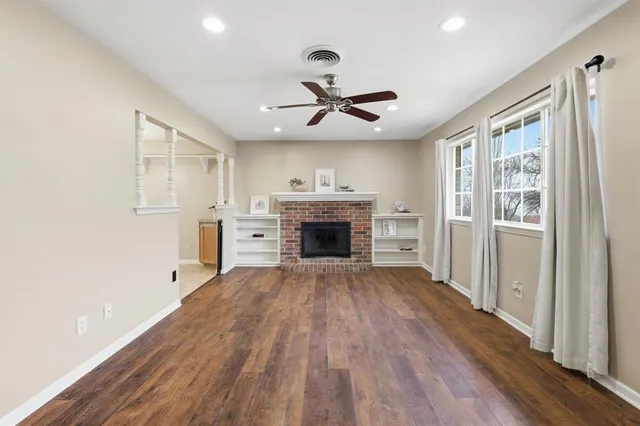 a view of a livingroom with a fireplace a ceiling fan and wooden floor