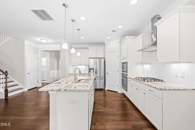 a large kitchen with kitchen island a stove a sink a refrigerator and white cabinets with wooden floor