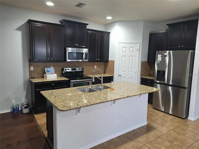 a kitchen with kitchen island granite countertop stainless steel appliances a refrigerator a stove a sink and a refrigerator