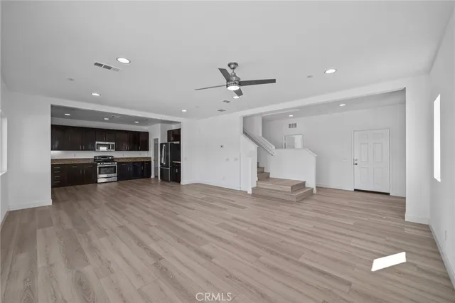 an empty room with wooden floor a ceiling fan and windows