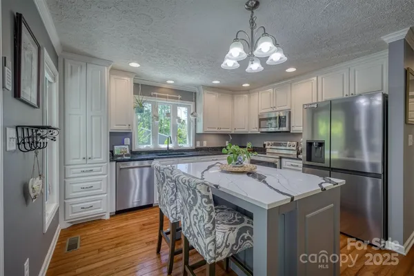 a kitchen with stainless steel appliances granite countertop a kitchen island hardwood floor sink stove dining table and chairs