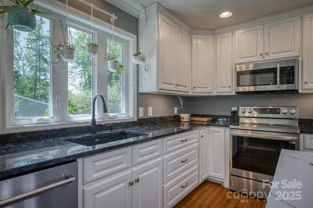 a kitchen with granite countertop a sink stainless steel appliances white cabinets and a window