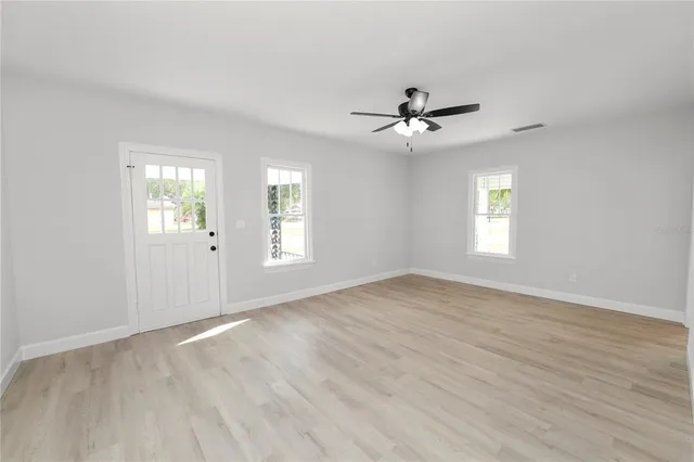 an empty room with wooden floor ceiling fan and windows