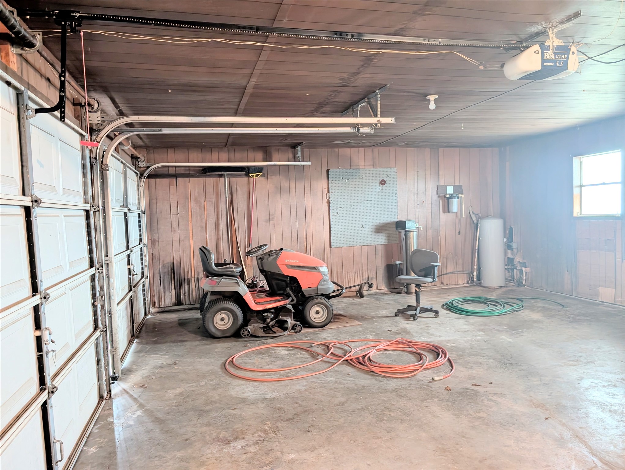 4779 Mixville Road Sealy, TX 77474 - Photo 30 of 47 Spacious attached 2 car garage features a double-door entry, concrete floor, and wood-paneled walls. It includes built-in shelving, a window for natural light, and ample room for storage or a workshop.