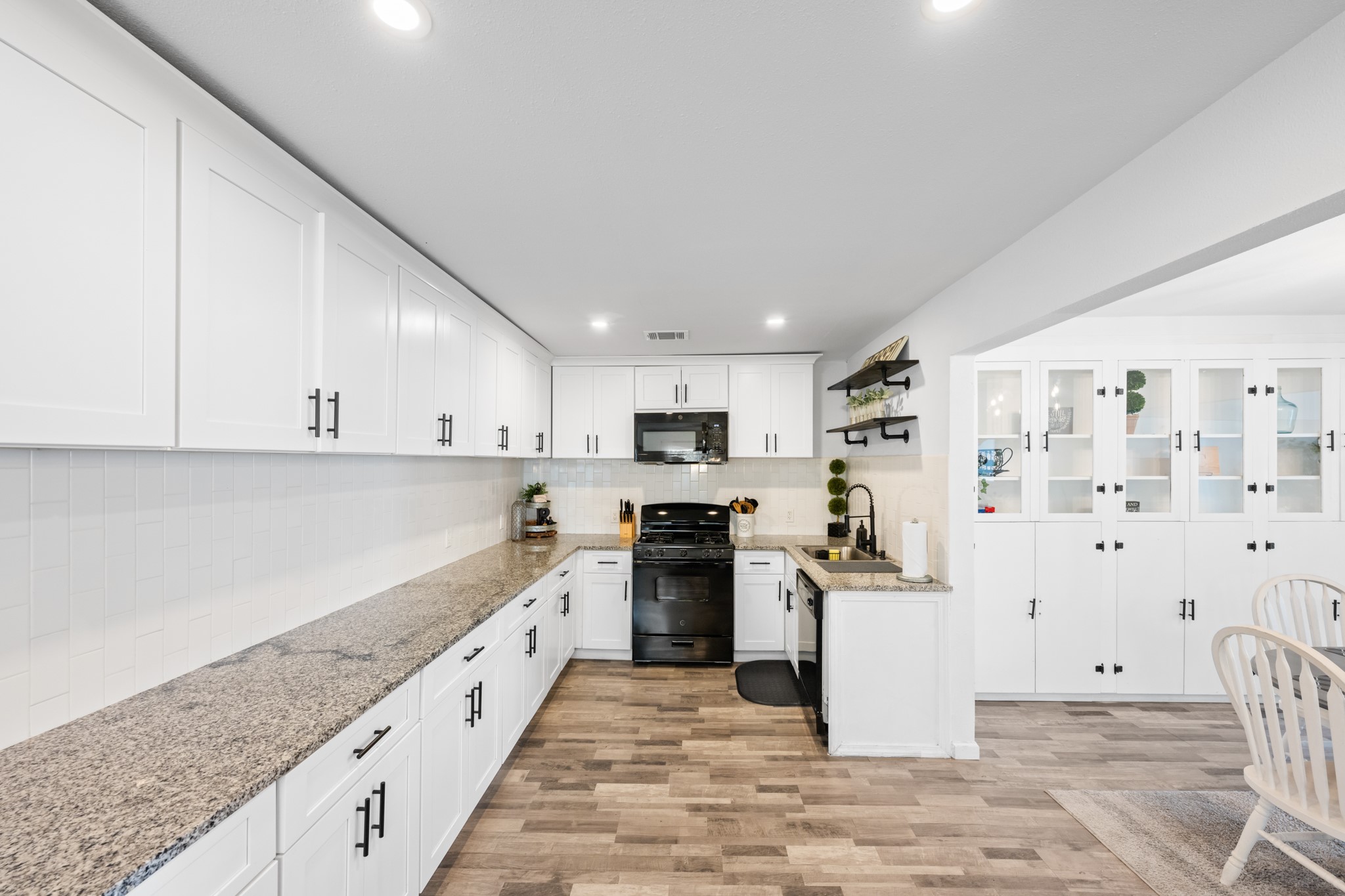 729 Kyle Angleton, TX 77515 - Photo 10 of 36 This kitchen features modern white cabinetry, granite countertops, and sleek black appliances. The open layout includes ample storage, a spacious dining area, and bright lighting, creating an inviting cooking and dining space.