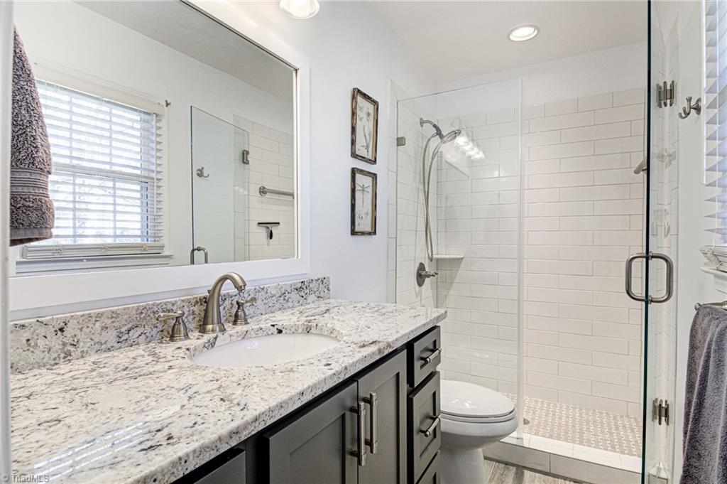 4516 Tower Road Greensboro, NC 27410 - Photo 18 of 26 Renovated main/primary bathroom boasts granite counters, elongated whtie subway tile, and frameless glass door