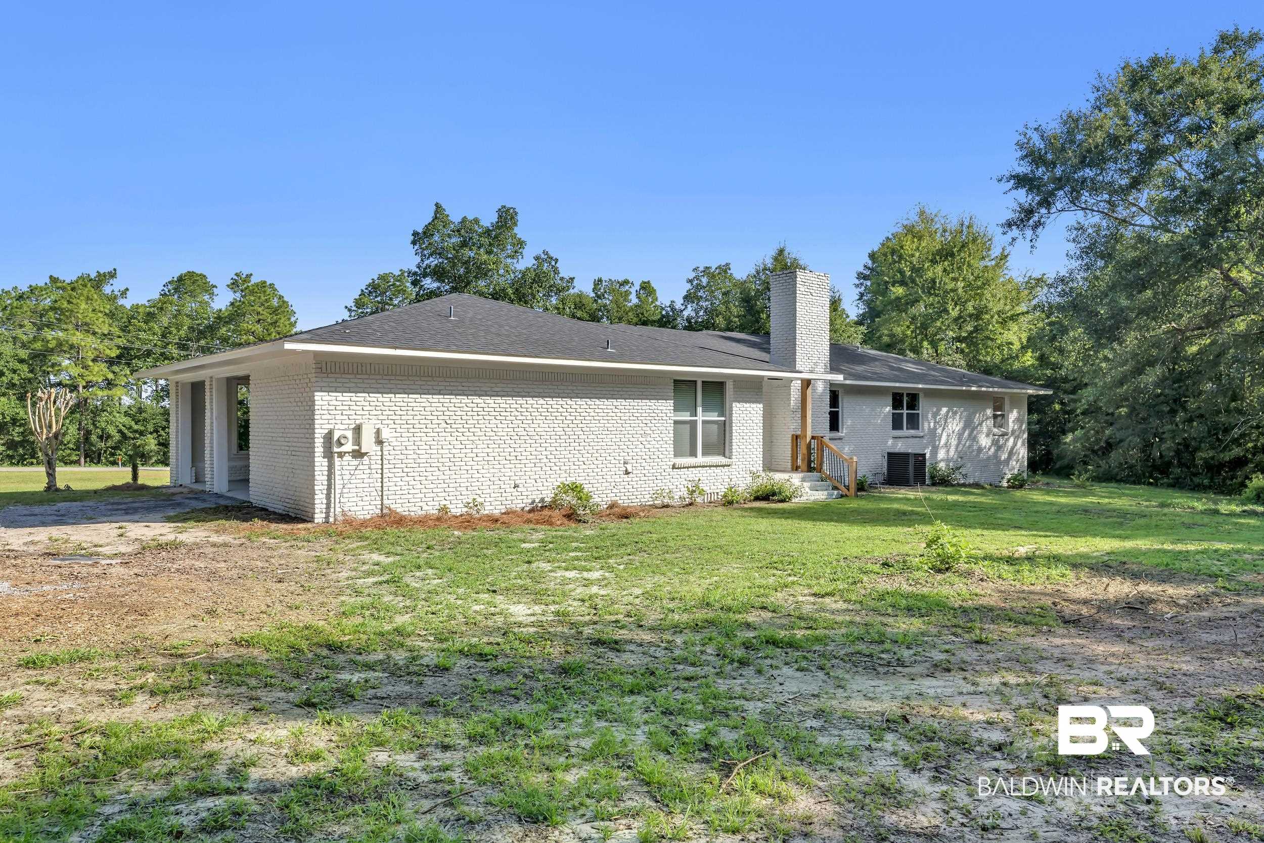 8170 Wilmer Georgetown Road Wilmer, AL 36587 - Photo 26 of 31 White brick exterior featuring a dark shingle roof, a covered patio area, and a prominent chimney