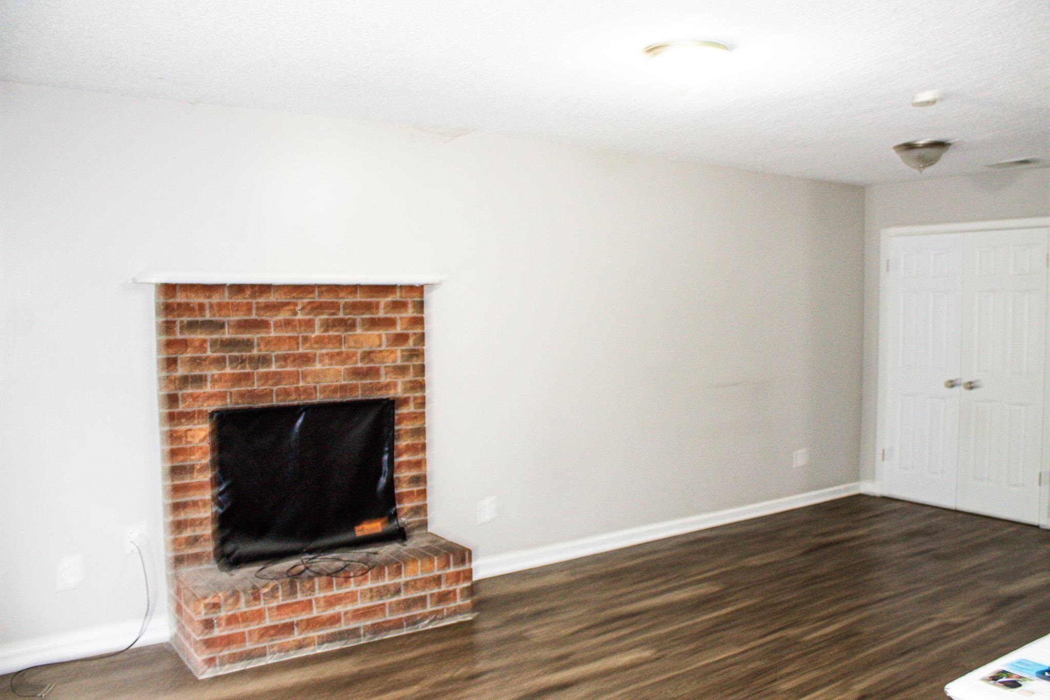 3592 Christine Road Memphis, TN 38118 - Photo 11 of 13 Brick fireplace with white mantel and hearth, wood-finish flooring, light grey painted walls, white baseboards, and double white closet doors