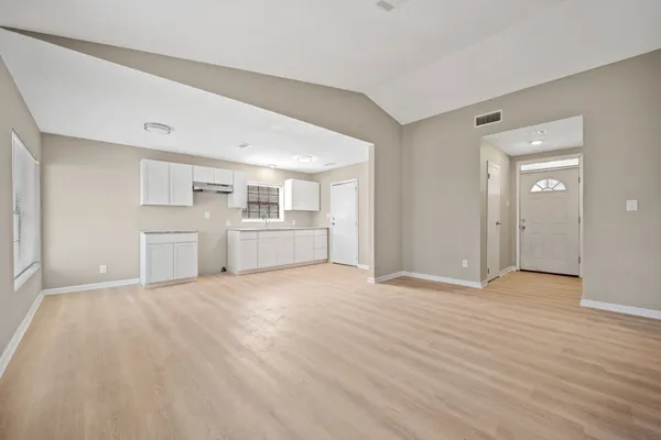 an empty room with wooden floor kitchen view and windows
