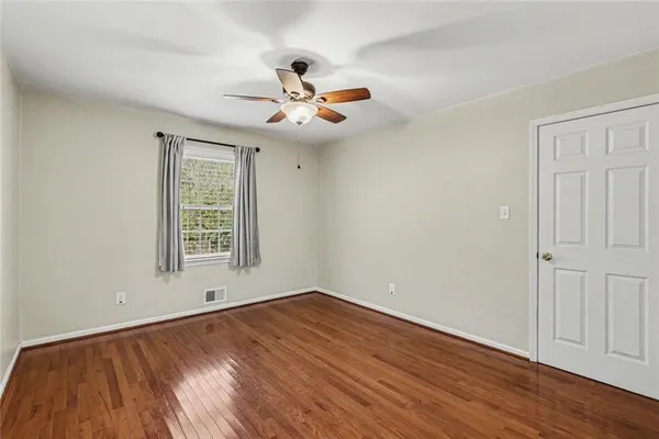 an empty room with wooden floor chandelier fan and windows