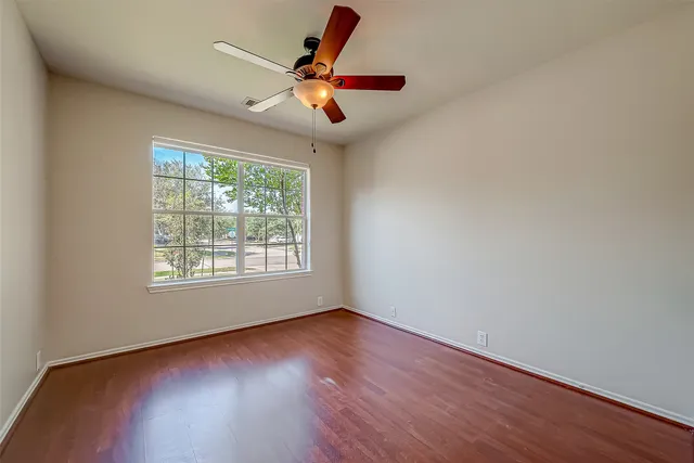 an empty room with wooden floor fan and windows