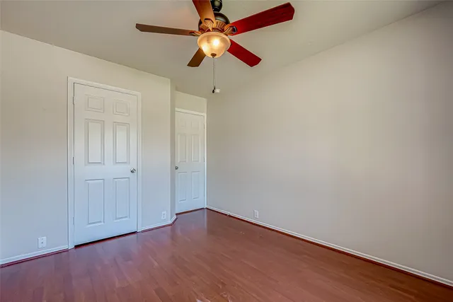 an empty room with wooden floor closet and fan