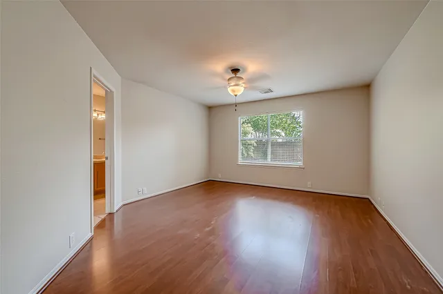 an empty room with wooden floor chandelier fan and windows