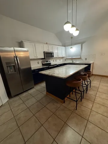 a kitchen with stainless steel appliances granite countertop a sink a stove a refrigerator a microwave oven with white cabinets and a granite counter top
