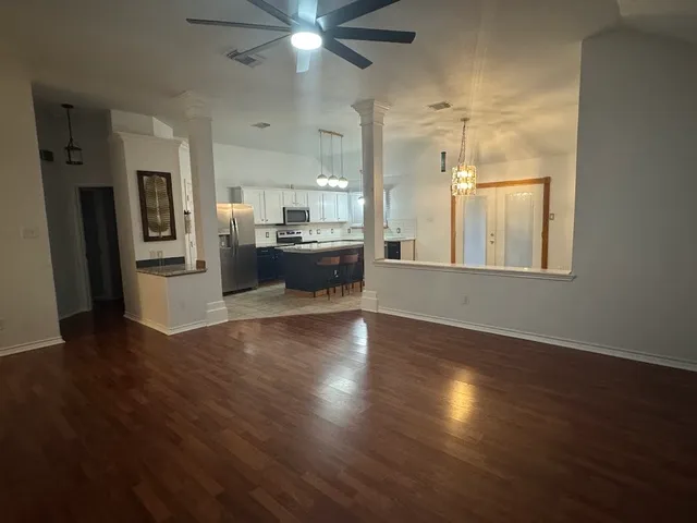 an empty room with wooden floor and a kitchen