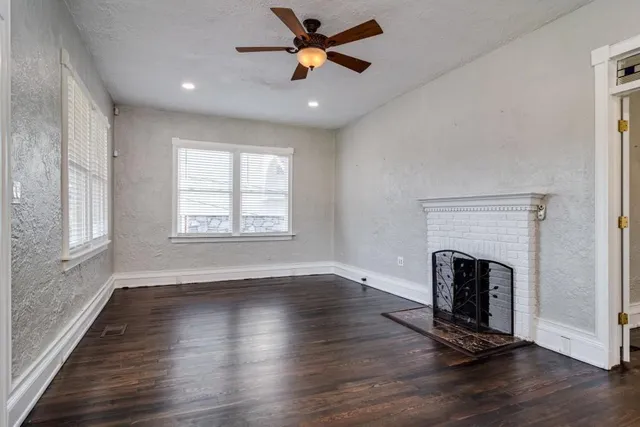 an empty room with wooden floor fireplace and windows