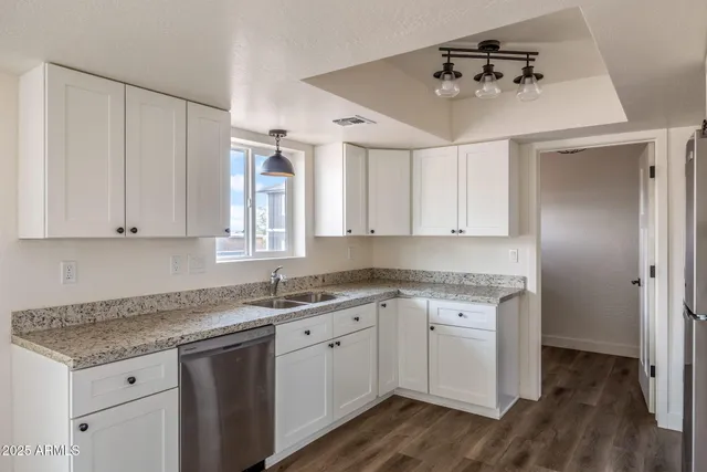 a kitchen with a sink dishwasher and white cabinets with wooden floor